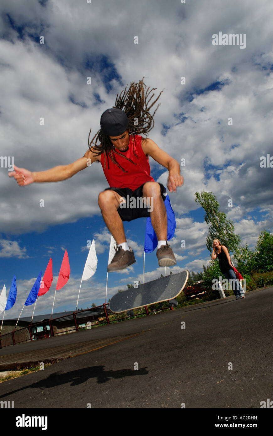 Skateboarder Airborne mâle noir avec des dreadlocks impressionnant fille blanche en arrière-plan Bend Oregon USA Banque D'Images