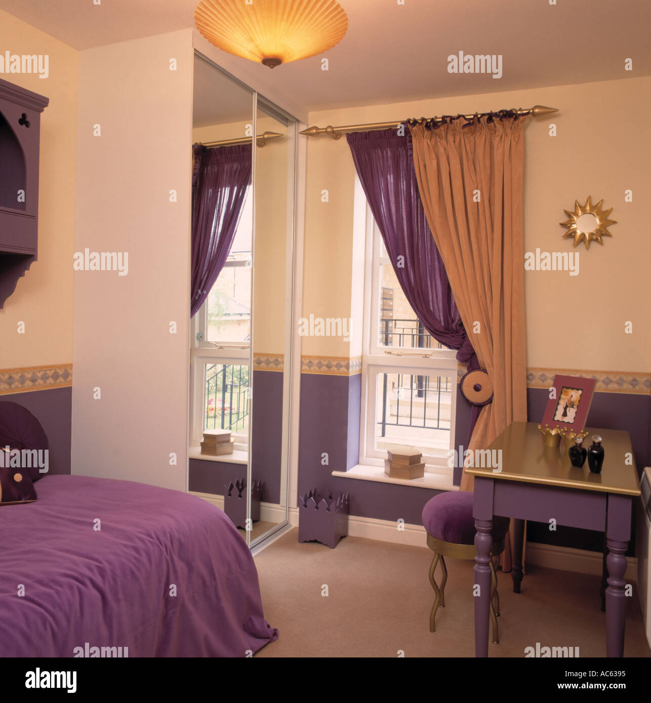 Violet et or à côté de la fenêtre à rideaux armoire équipée avec porte miroir dans l'appartement avec chambre à coucher couvre-lit pourpre Banque D'Images