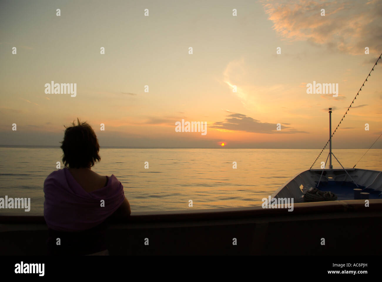 Ciel coucher de soleil et silhouette de femme sur le pont des passagers à l'avant de navire de croisière en mer Ionienne tranquille calme en regardant un coucher de soleil sous l'horizon drop Banque D'Images