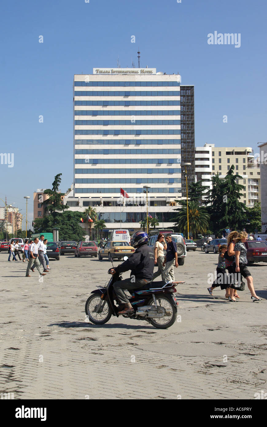 Scène de rue en République d'Albanie Tirana, la place Skanderbeg cyclomoteur en esquivant de poule personnes traversant route multi histoire Tirana International Hotel beyond Banque D'Images Scène de rue en République d'Albanie Tirana, la place Skanderbeg cyclomoteur en esquivant de poule personnes traversant route multi histoire Tirana International Hotel beyond Banque D'Images