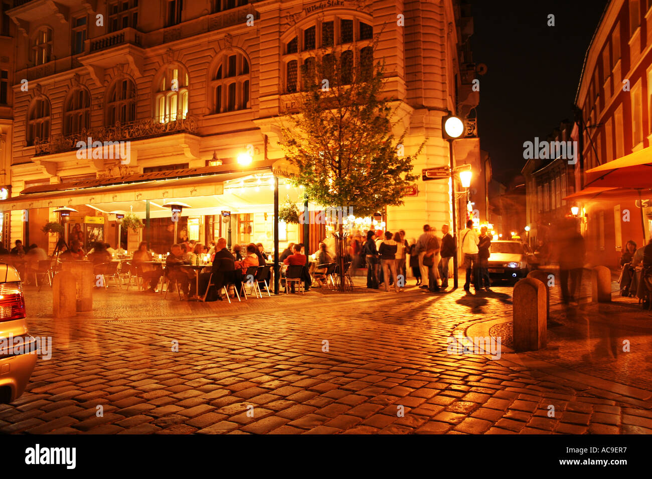 Scène nocturne de Prague avec une rue animée, des repas en plein air et des gens réunis autour de bâtiments illuminés créant une atmosphère animée et vibrante. Banque D'Images