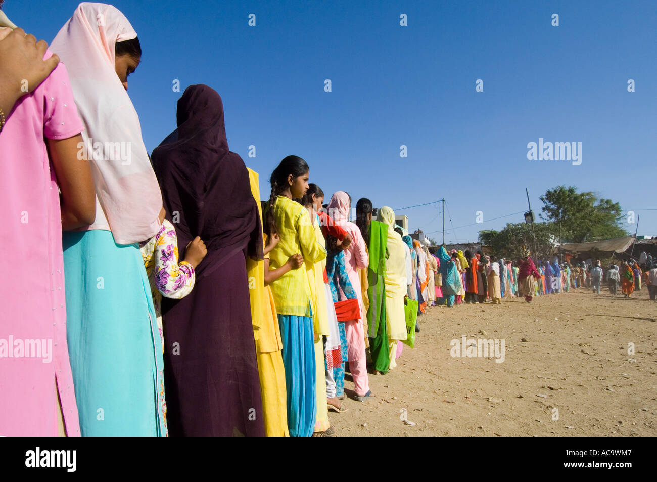 Une longue file d'attente des femmes et des jeunes filles vêtues de leurs plus beaux vêtements attendre patiemment la nourriture gratuite au Mewar festival. Banque D'Images