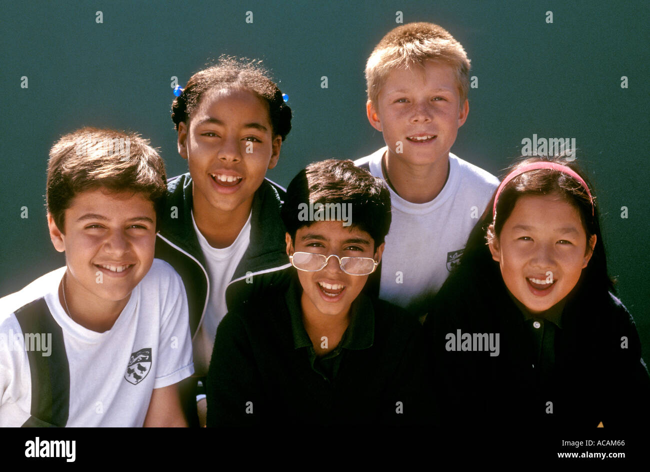 Groupe de société multiraciale happy smiling junior school les élèves à l'extérieur sous le soleil de jeux avec mur derrière sport verte Banque D'Images