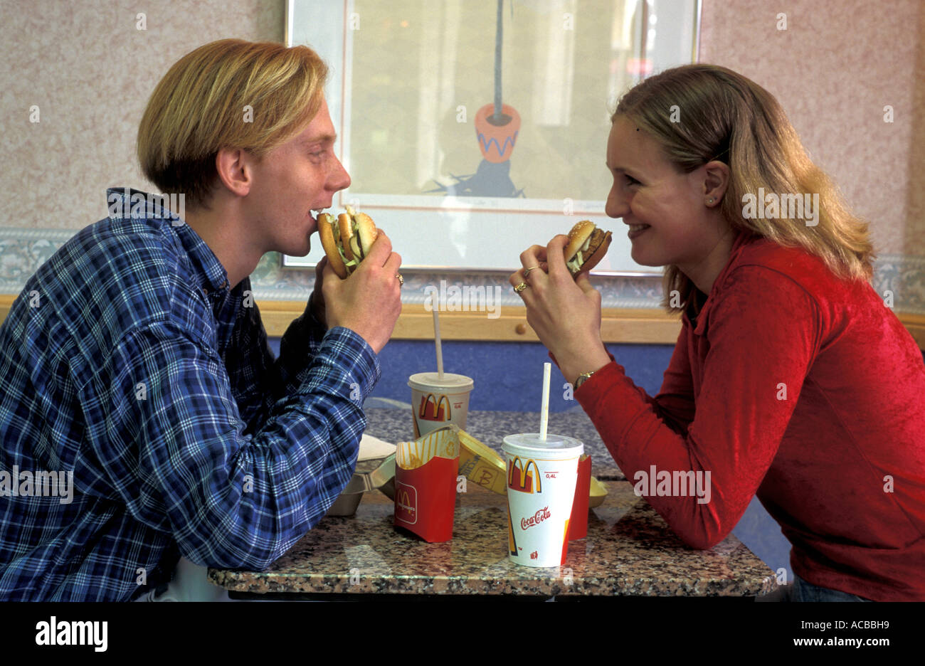 Teenage couple sitting at table in fast food eating hamburger et frites Banque D'Images