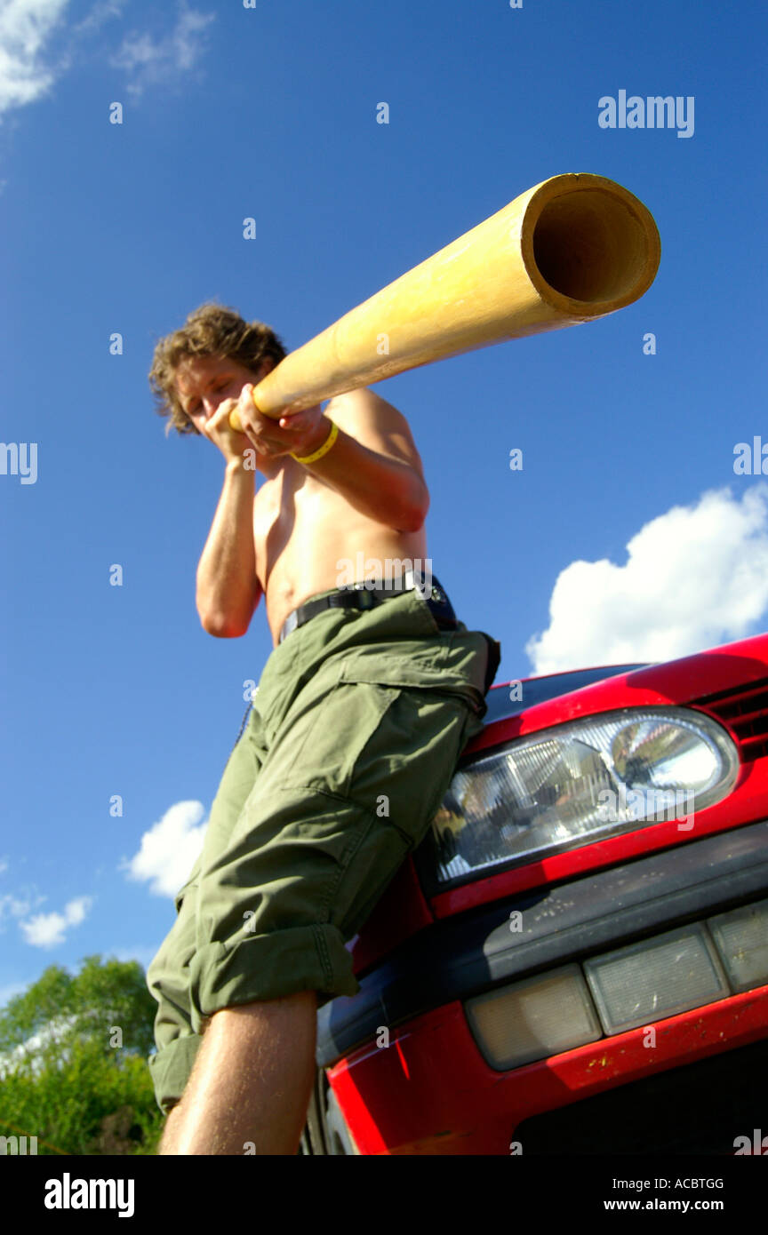Poitrine nue young man blowing didgeridoo en bois énorme à l'extérieur sous ciel bleu Banque D'Images