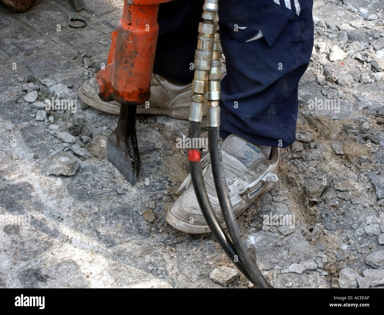 Un travail ouvrier perceuse à air comprimé pour briser cobble stone road portant des chaussures inappropriées whist Banque D'Images