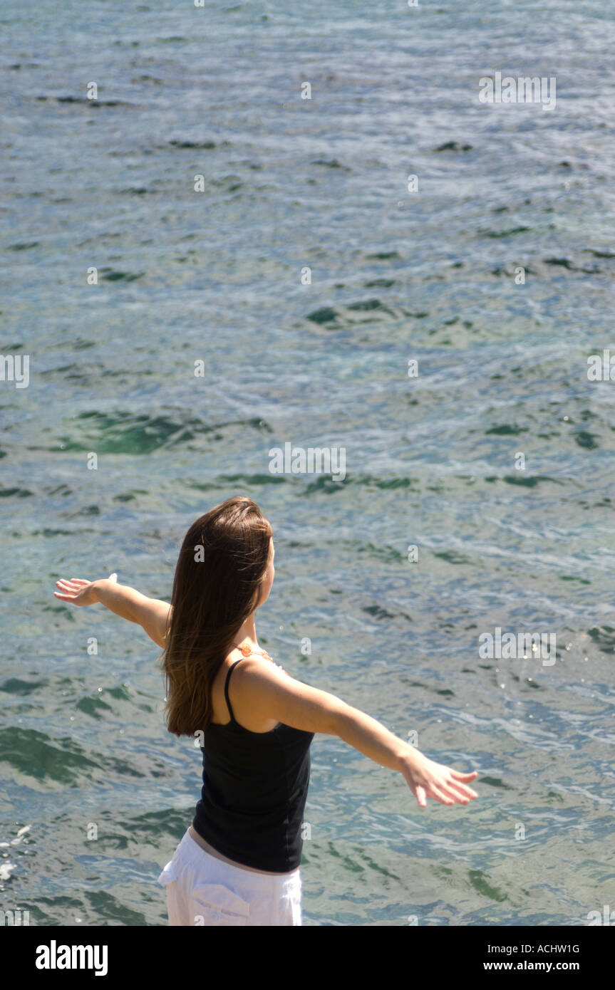 Sliim red haired young woman standing by the sea bras tendus au soleil vêtu de noir veste et pantalon blanc pantalons Banque D'Images