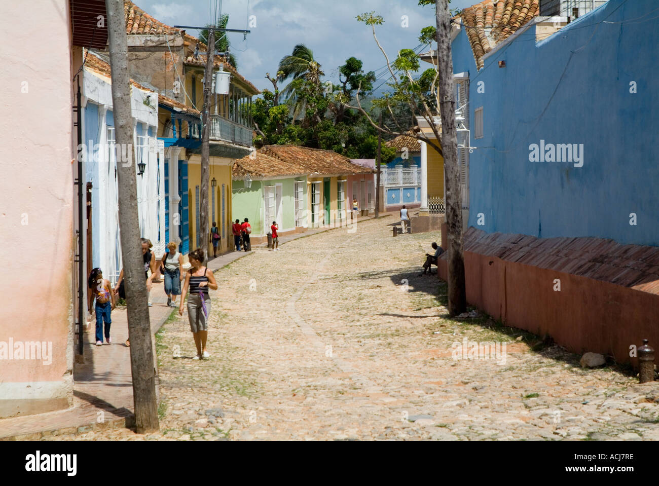 Couple walking passé windows avec des grilles métalliques sur une rue pavée, Trinidad, Cuba. Banque D'Images