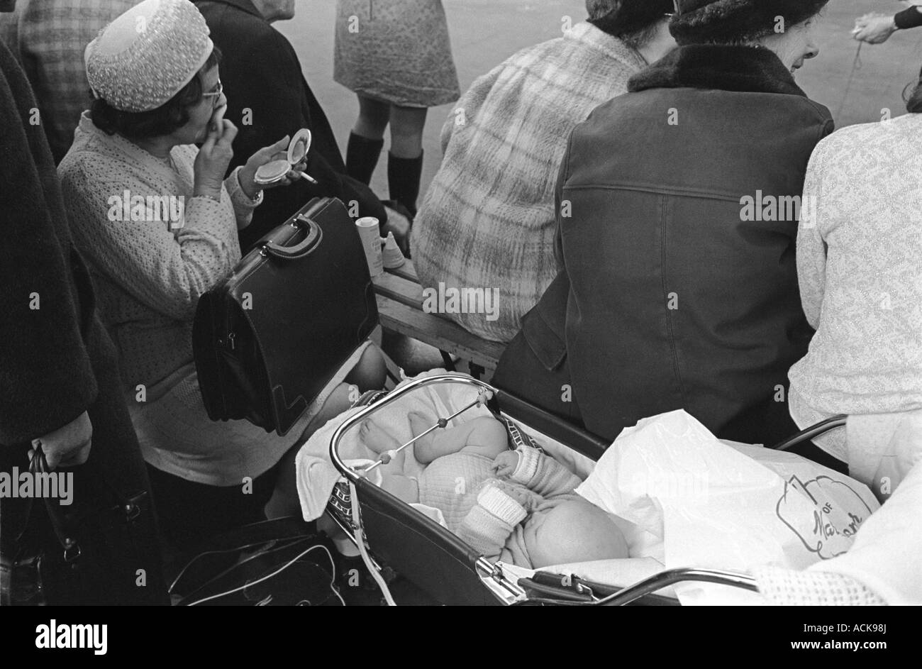 Mère plus âgée avec son bébé dans un pram, femme mettant son maquillage en public, tenant le miroir de main et fumant Londres années 1970 UK HOMER SYKES Banque D'Images
