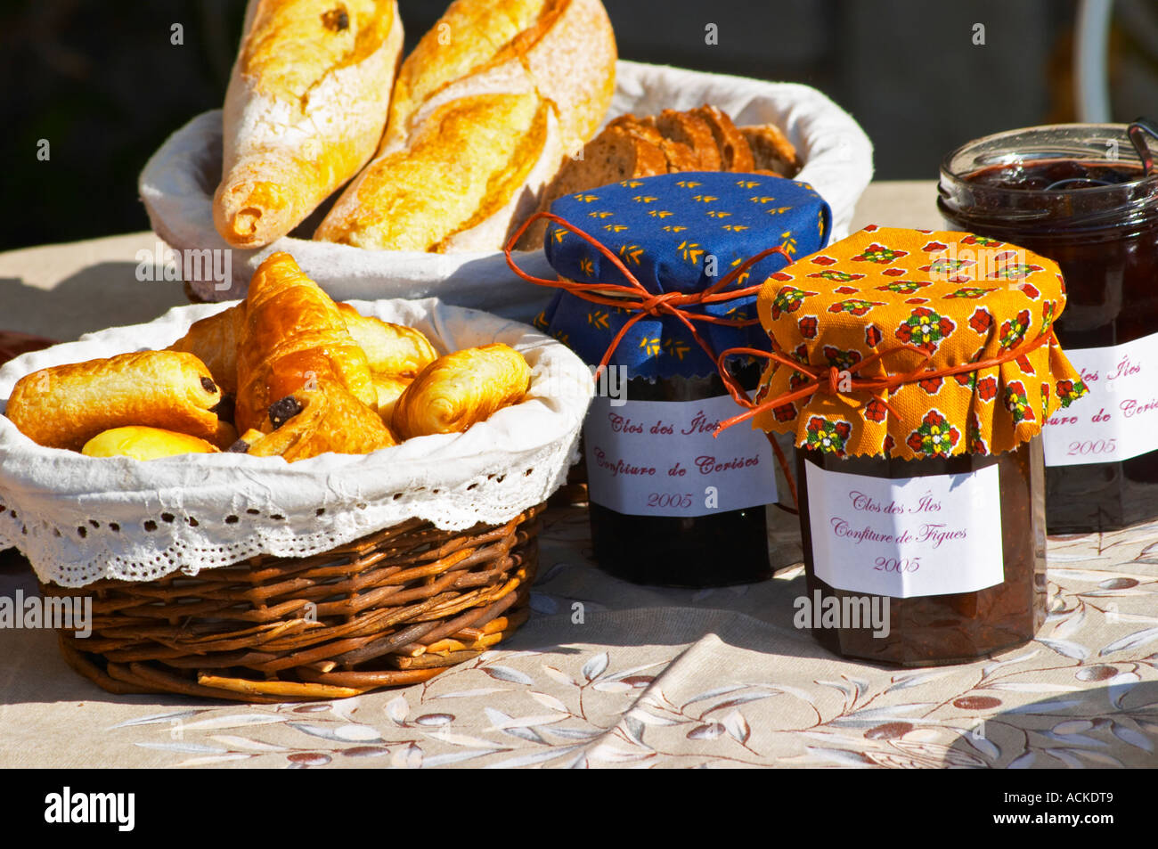 Un petit-déjeuner panier en osier avec des croissants et pains au chocolat, (pain au chocolat) bocaux pots de confiture Confiture confiture de fruits et de baies couvertes de tissu provençal coloré panier de pain baguette Clos des Iles Le Brusc Six Fours Côte d'Azur Var France Banque D'Images