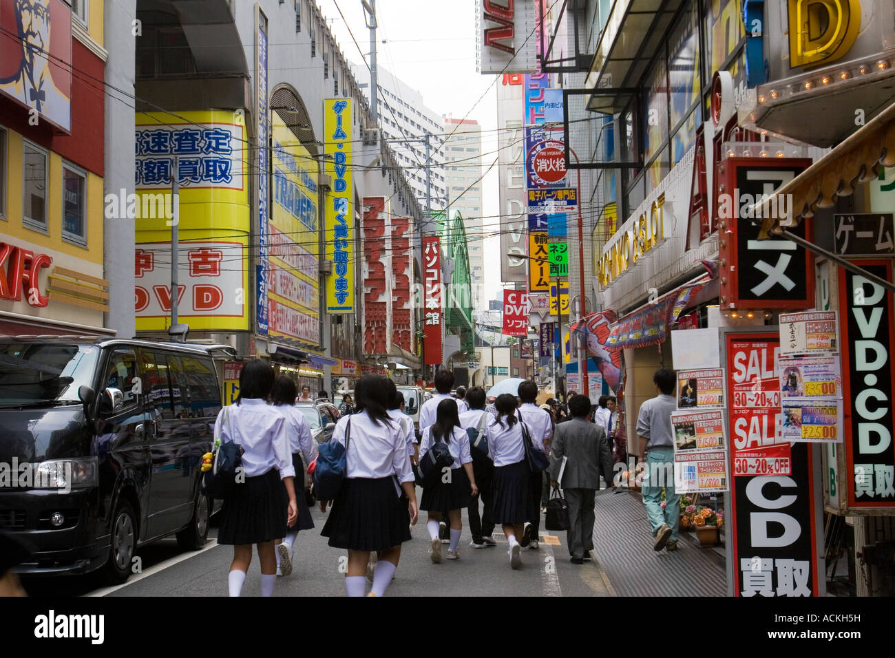 Filles de l'école de porter des uniformes marcher dans une rue animée avec des annonces dans l'électronique d'Akihabara district de Tokyo Japon Banque D'Images