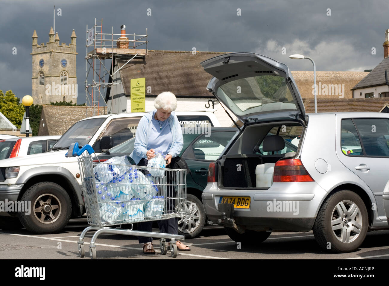 Bouteilles bouteille femme chargement en eau potable chariot de supermarché Tesco parc voiture Gloucestershire UK Cleeve Évêques Banque D'Images