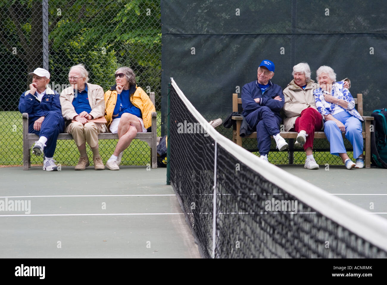 Les hommes et les femmes retraités âgés assis sur des bancs à côté d'un filet de tennis à regarder un match en cours Banque D'Images