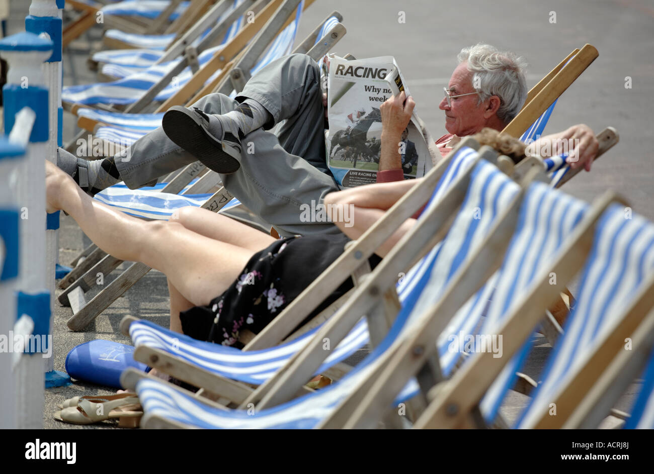 Un homme lisant le journal 'Post' de course alors qu'il était assis dans une chaise longue sur le front de mer de Weymouth UK Banque D'Images