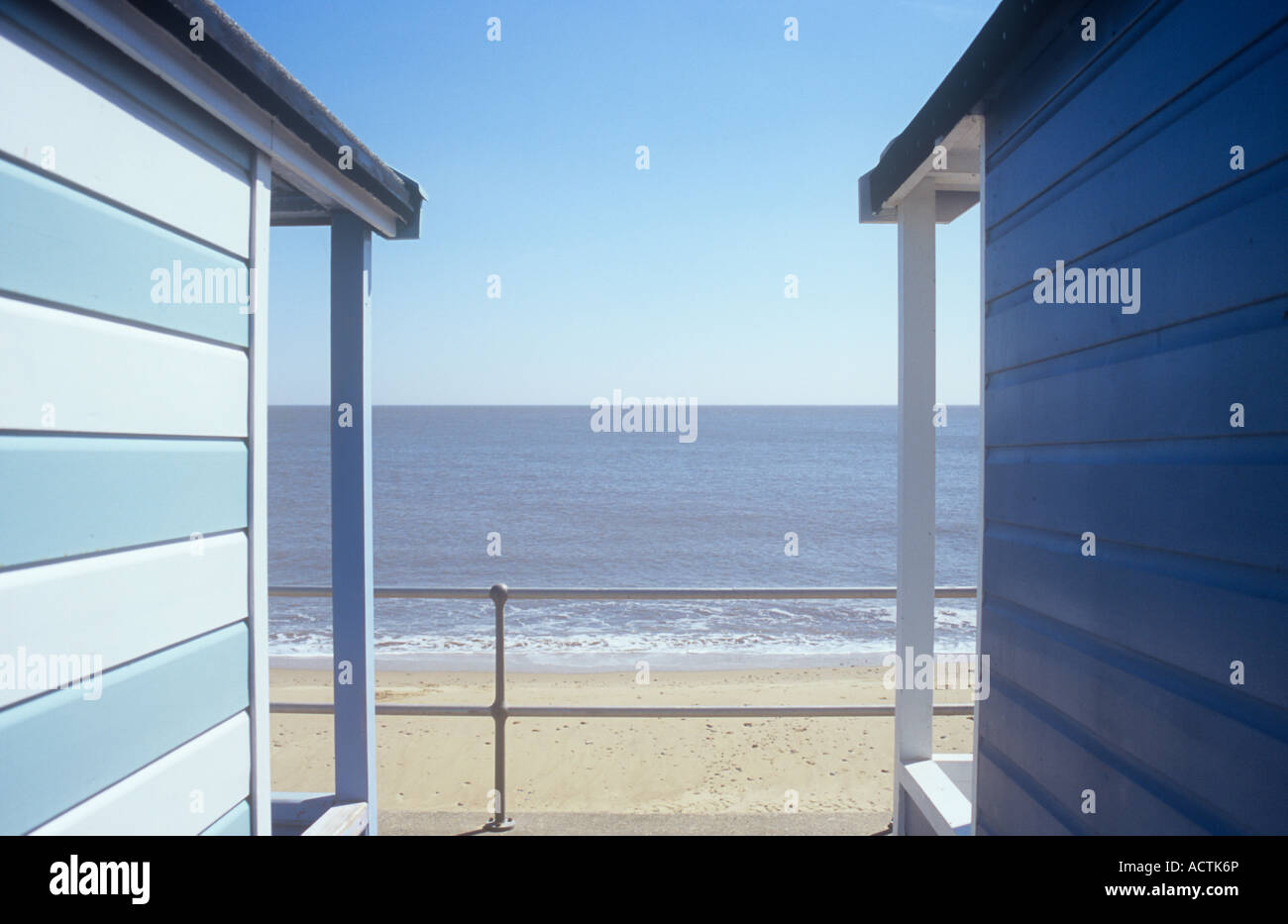 Voir entre deux cabanes de plage promenade vers les garde-corps avec nettoyage plage de sable ensoleillée et d''une mer calme et le ciel au-delà Banque D'Images