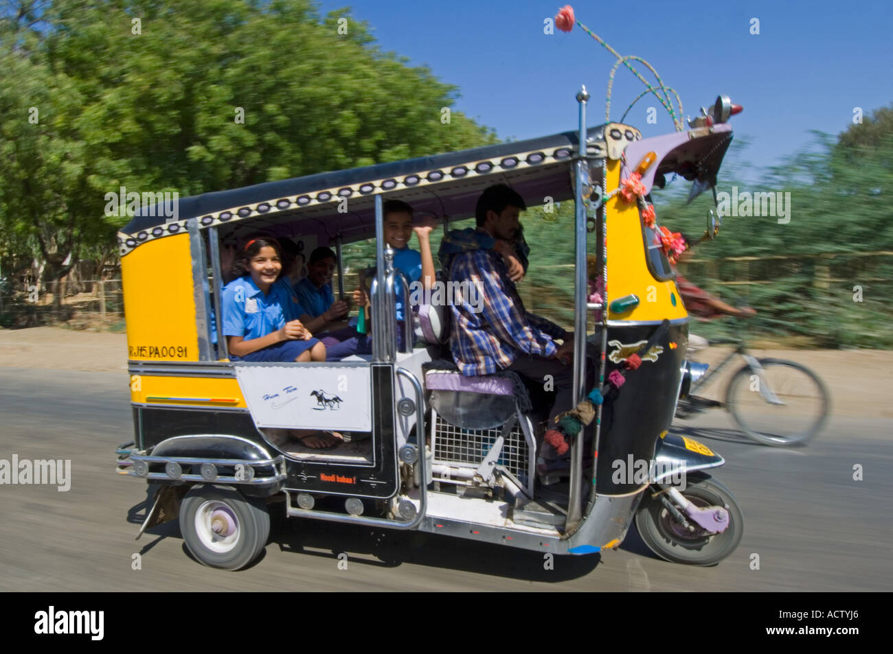 Un décoré de jaune et noir auto rickshaw (tuk tuk) avec les enfants de l'école sourire pris avec vitesse d'obturation lente pour le motion blur. Banque D'Images