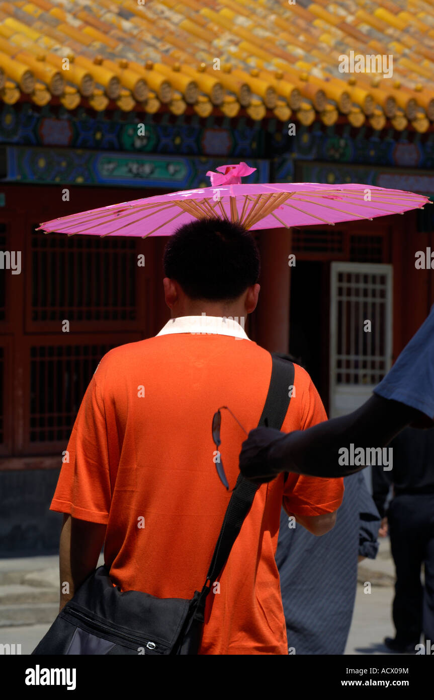 L'homme à un haut orange avec un parasol rose dans la Cité Interdite Banque D'Images