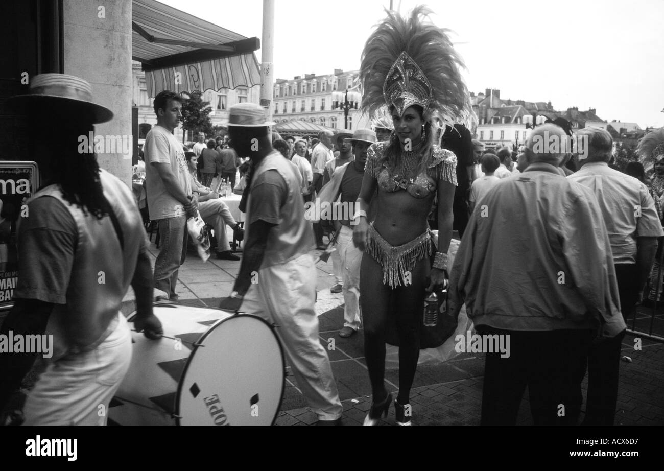 Le noir et blanc des membres de l'école de samba traverser une rue bondée sur leur retour d'une performance Banque D'Images