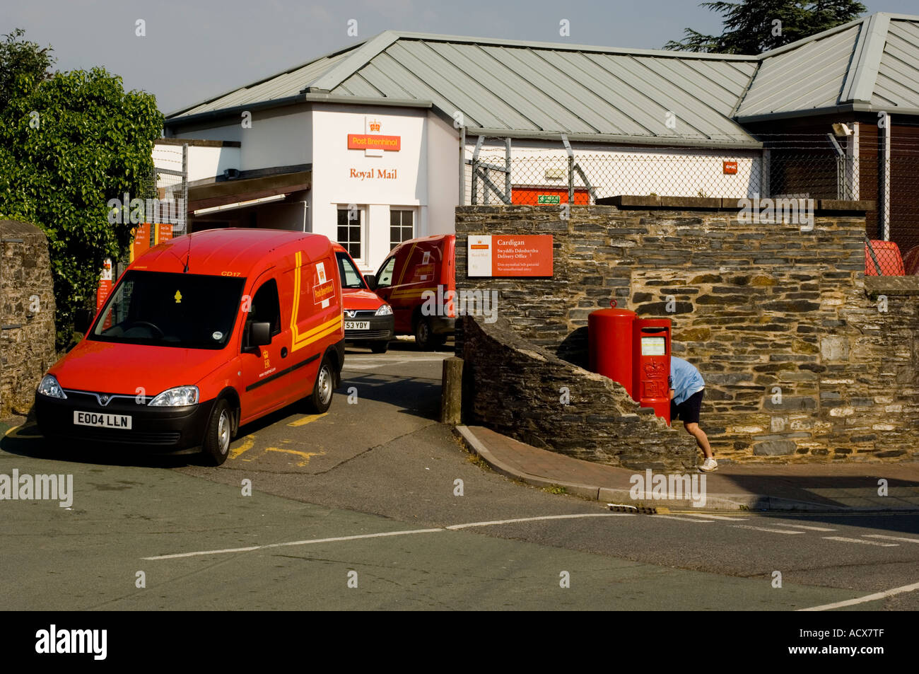 Postman la collecte des mail poster à partir d'une boîte à l'extérieur un dépôt postal Cardigan rouge avec van à proximité Banque D'Images