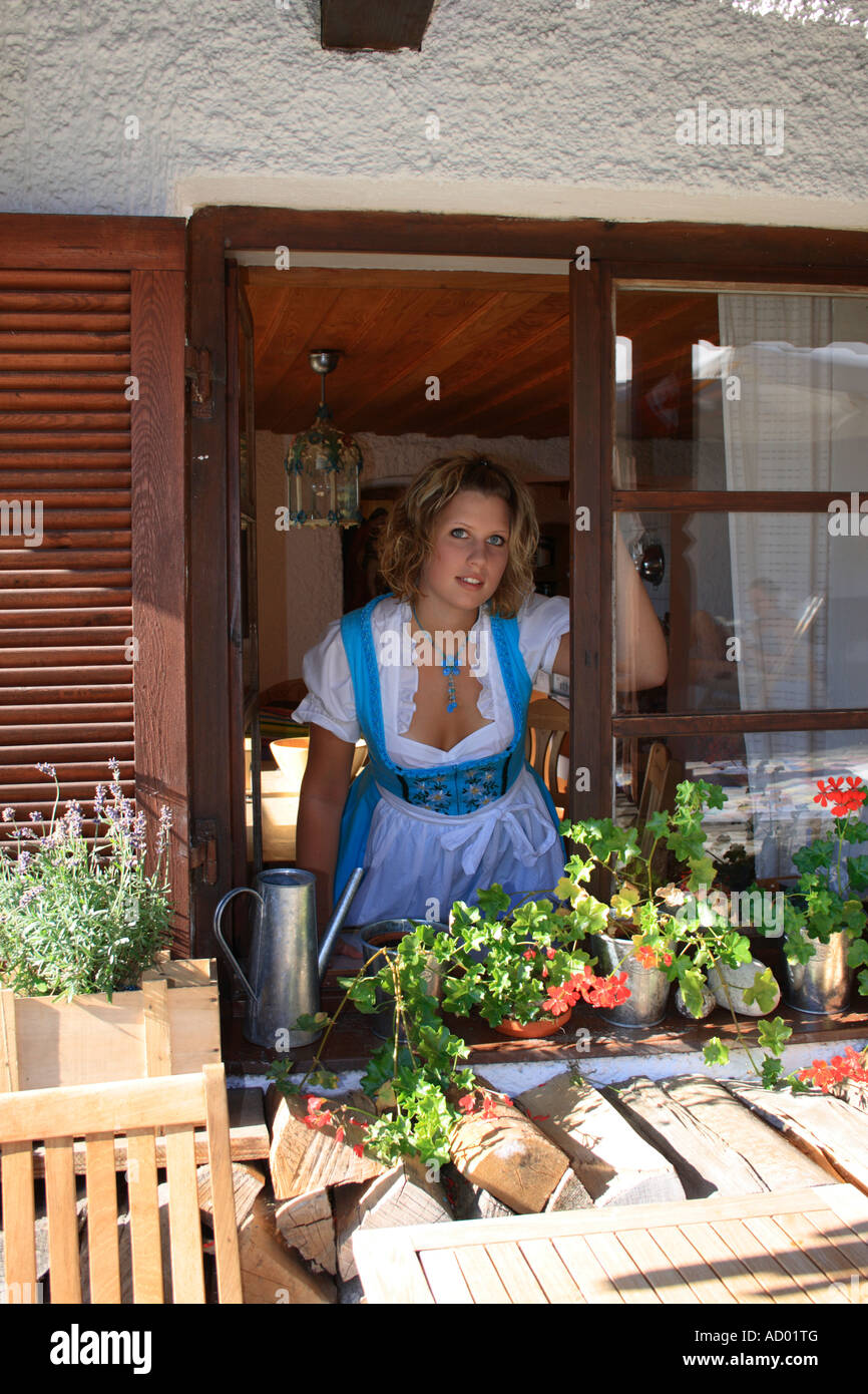 Jeune fille blonde en vêtements traditionnels bavarois (Dirndl) à la recherche d'une ancienne ferme la fenêtre. Photo par Willy Matheisl Banque D'Images