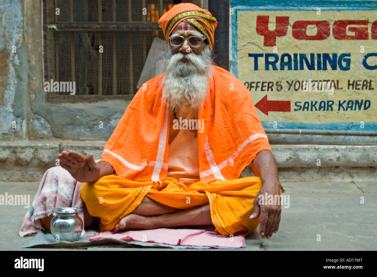 Portrait horizontal d'un vieux sadhu habillés en vêtements traditionnels safran assis en tailleur sur un trottoir. Banque D'Images