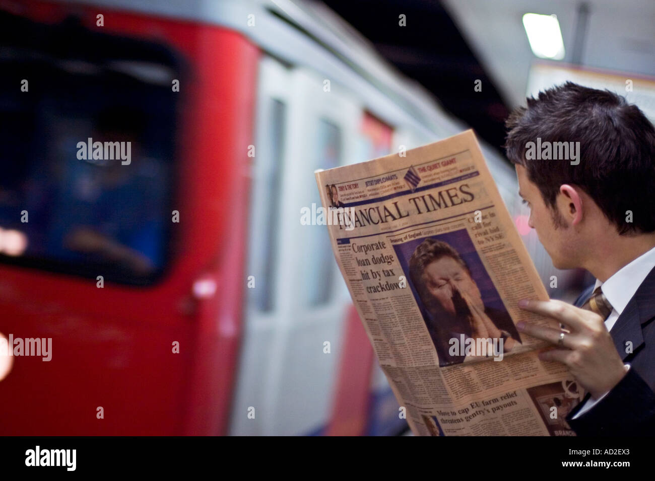 Jeune homme lit journal Financial Times sur la plate-forme du métro de Londres Banque D'Images