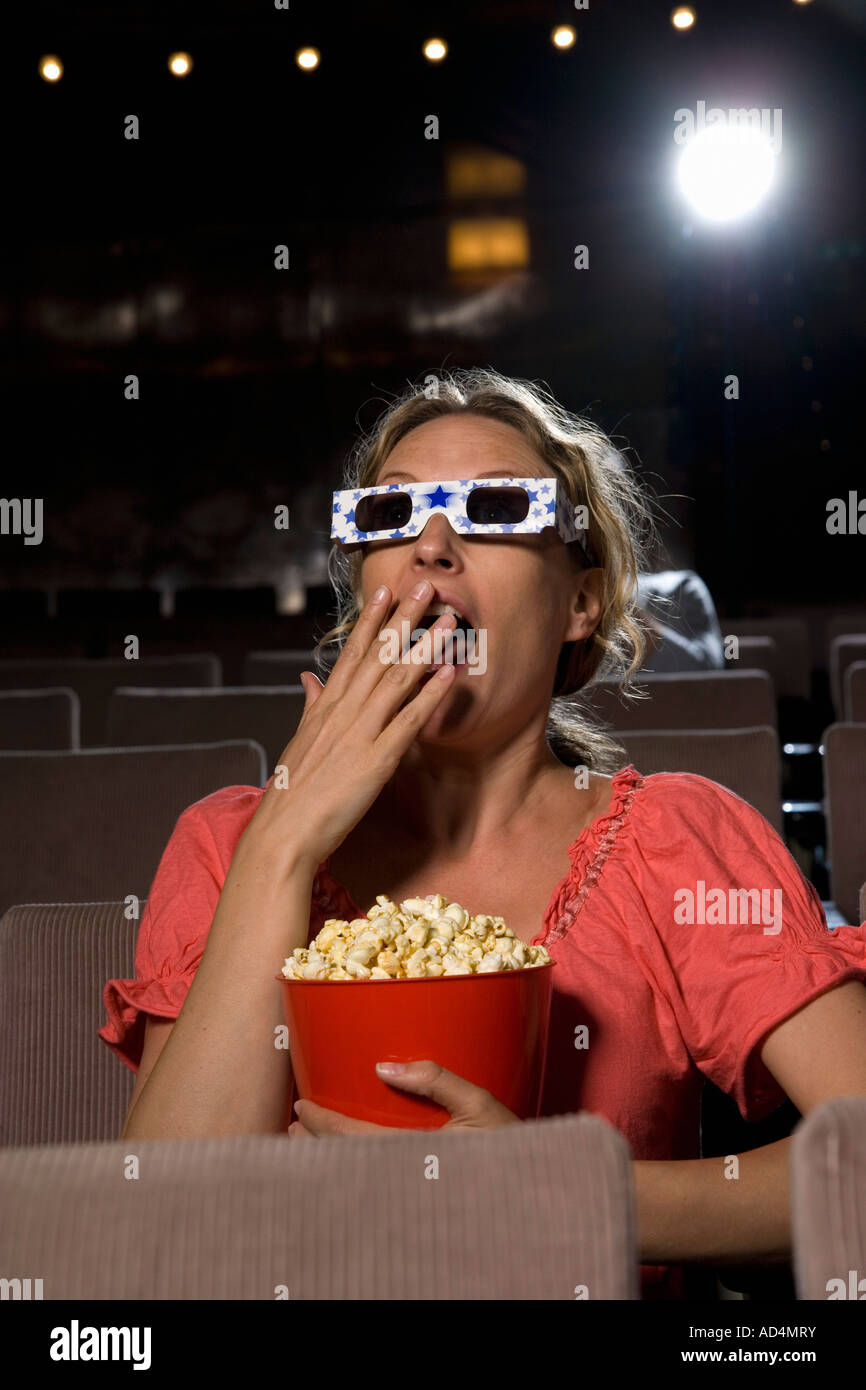 Une femme assise dans une salle de cinéma portant des lunettes 3-D et eating popcorn Banque D'Images