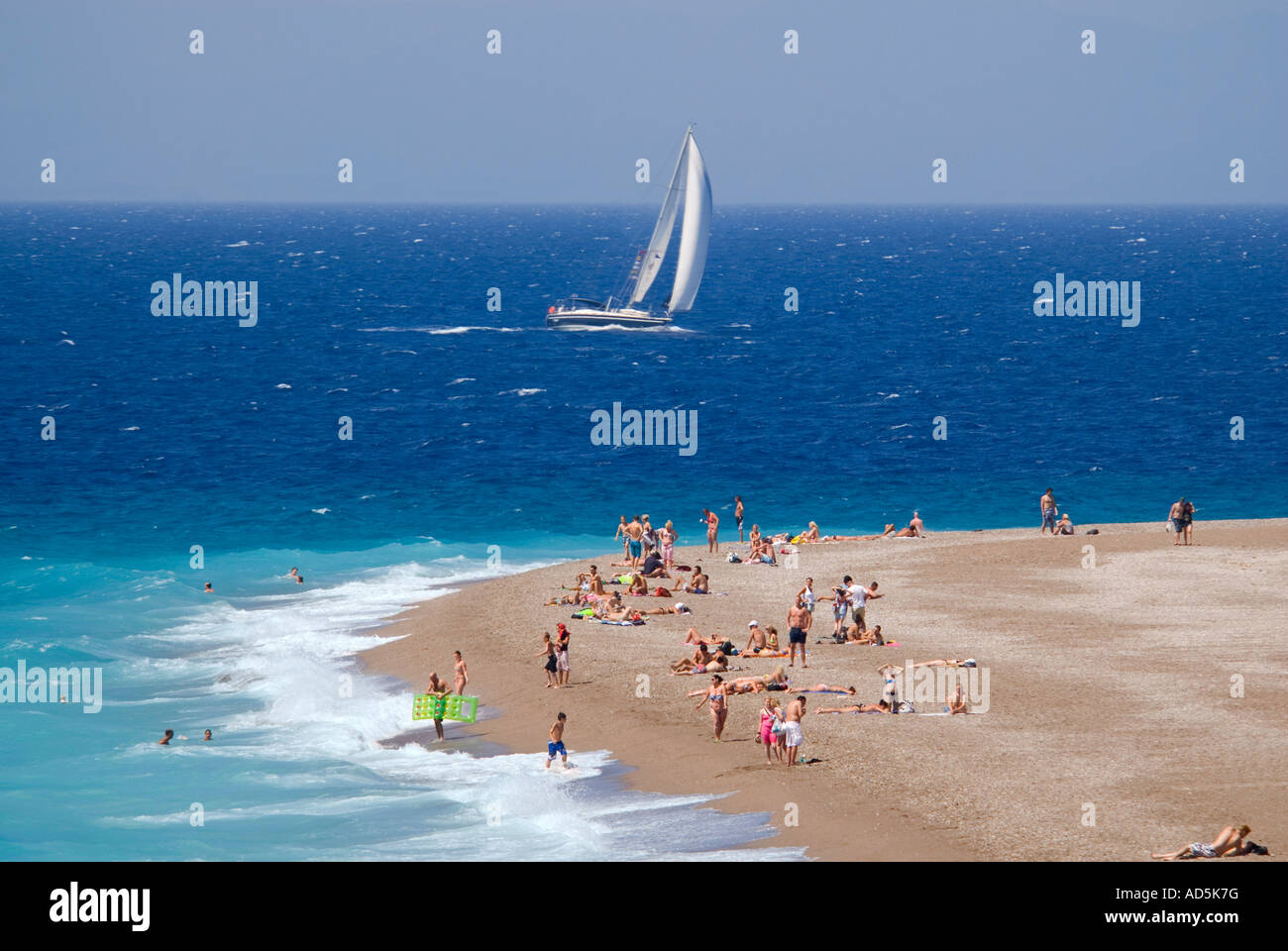 Vue aérienne horizontale des vacanciers sur la plage avec un yacht blanc voile passé au soleil. Banque D'Images