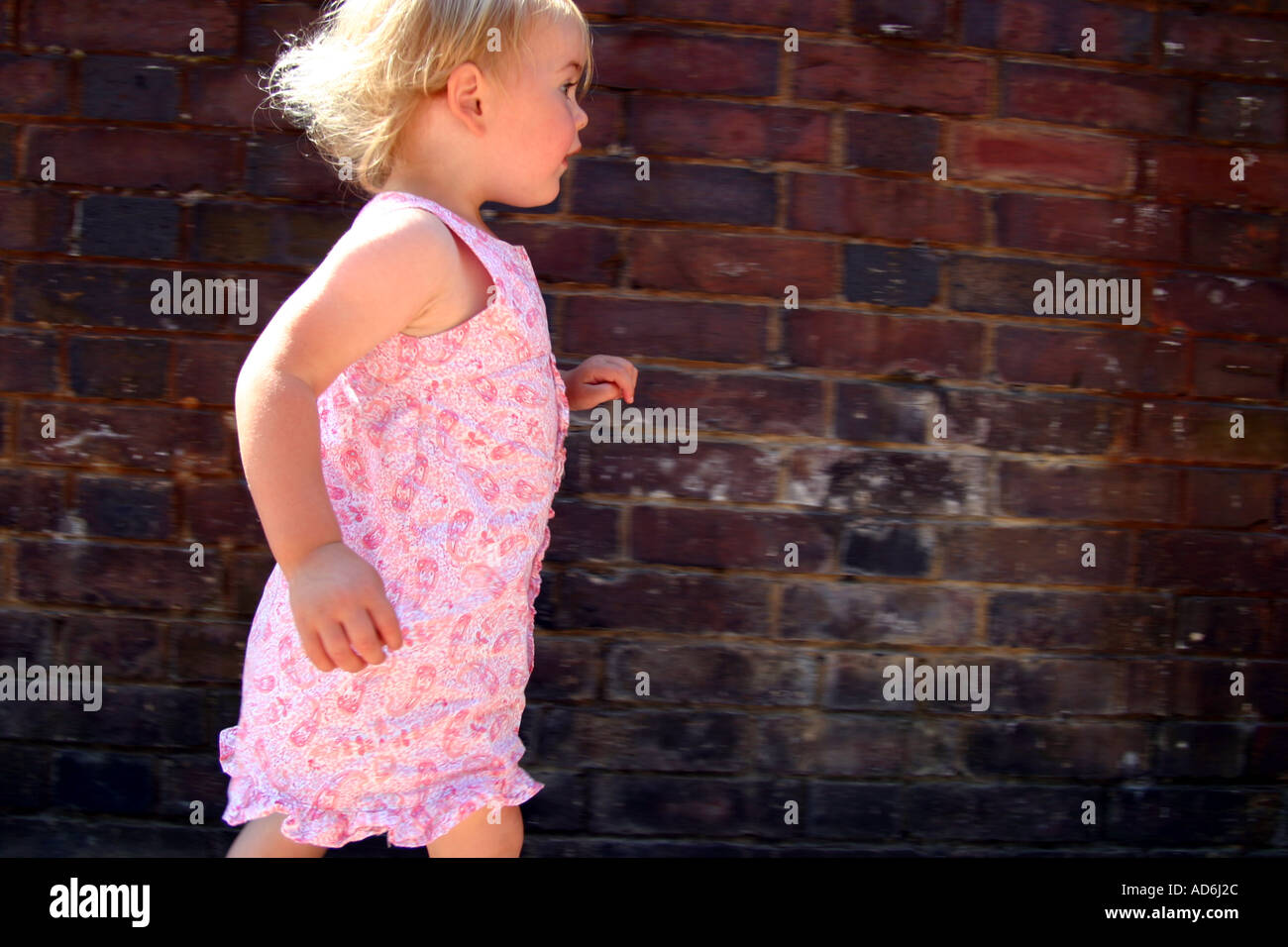 2 ans, fille, portant robe rose le long de mur sur un été chaud s jour Banque D'Images