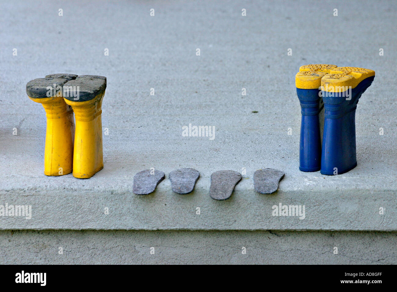 Bottes jaune et bleu à l'envers à l'écart sur un porche de béton gris à semelles sec parfaitement alignés entre eux Banque D'Images