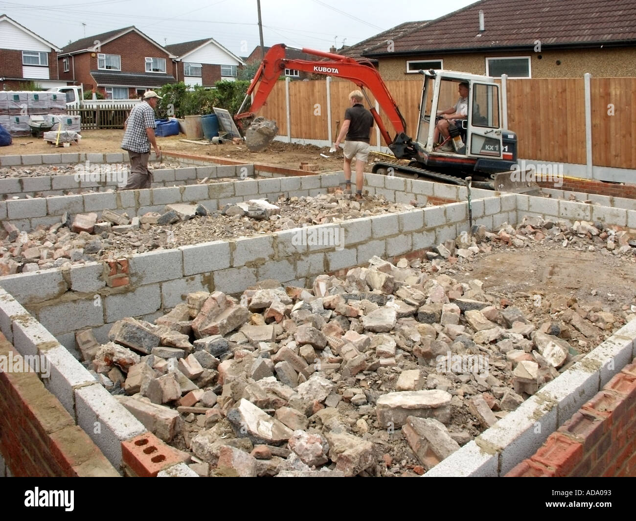 Pelle hydraulique Mini Digger & driver plaçant des décombres entre les blocs de béton des murs pour nouvelle maison sous-structure prête pour sol béton UK Banque D'Images