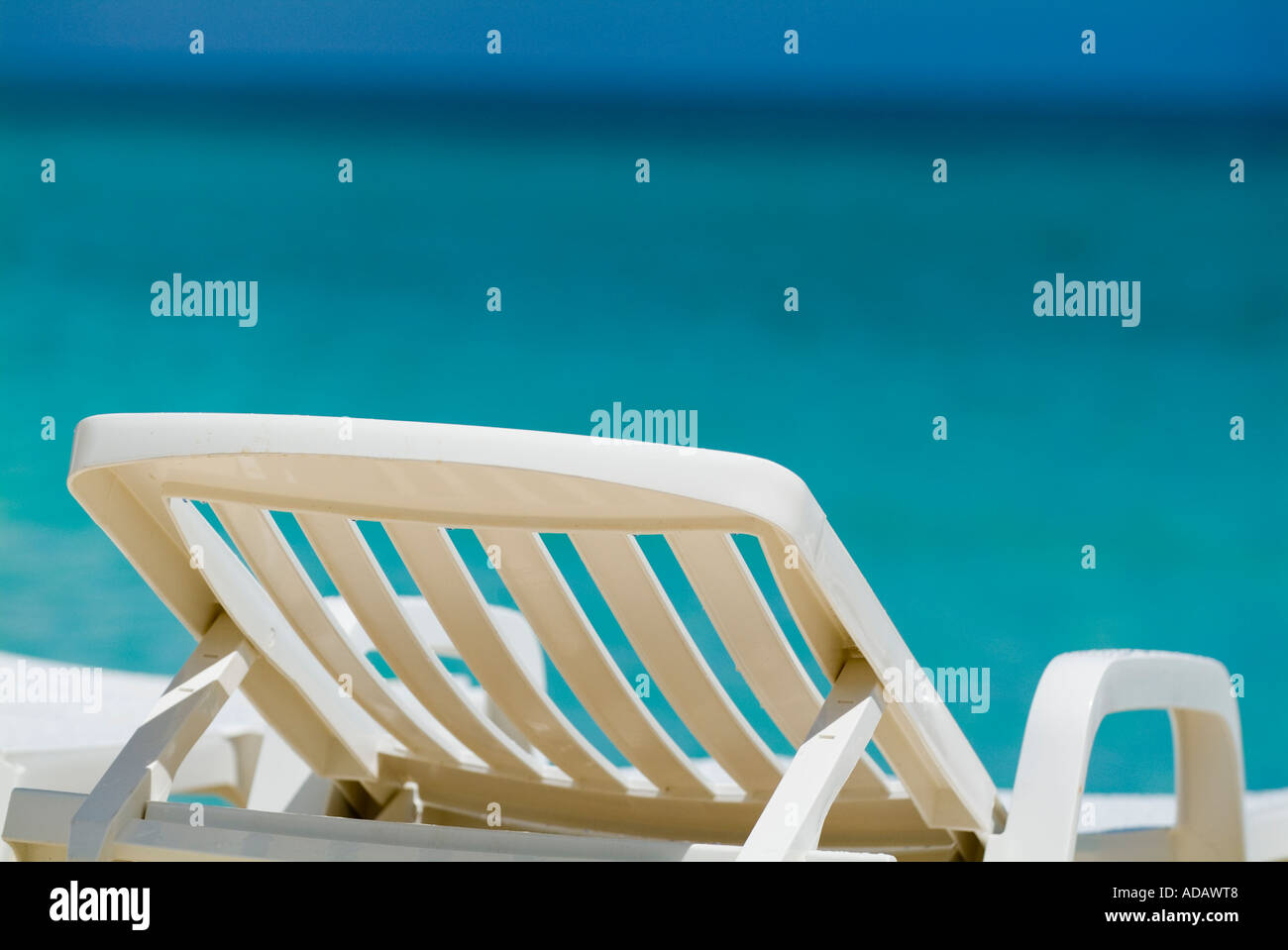 Chaise longue blanche vide / chaise longue sur une plage tropicale avec un océan bleu vif par une journée ensoleillée Banque D'Images