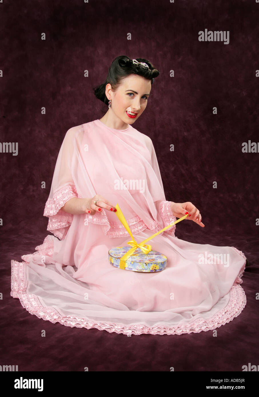 Pin Up Girl dans une robe rose d'ouvrir une boîte de bonbons attachés avec un ruban jaune Banque D'Images