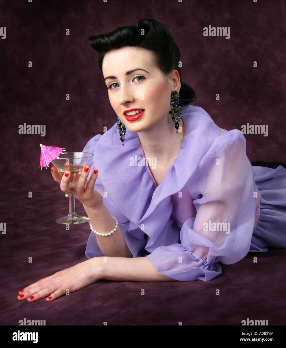 Un Pin Up Girl in a Purple Blouse tenant un verre à cocktail avec un parapluie Rose Banque D'Images