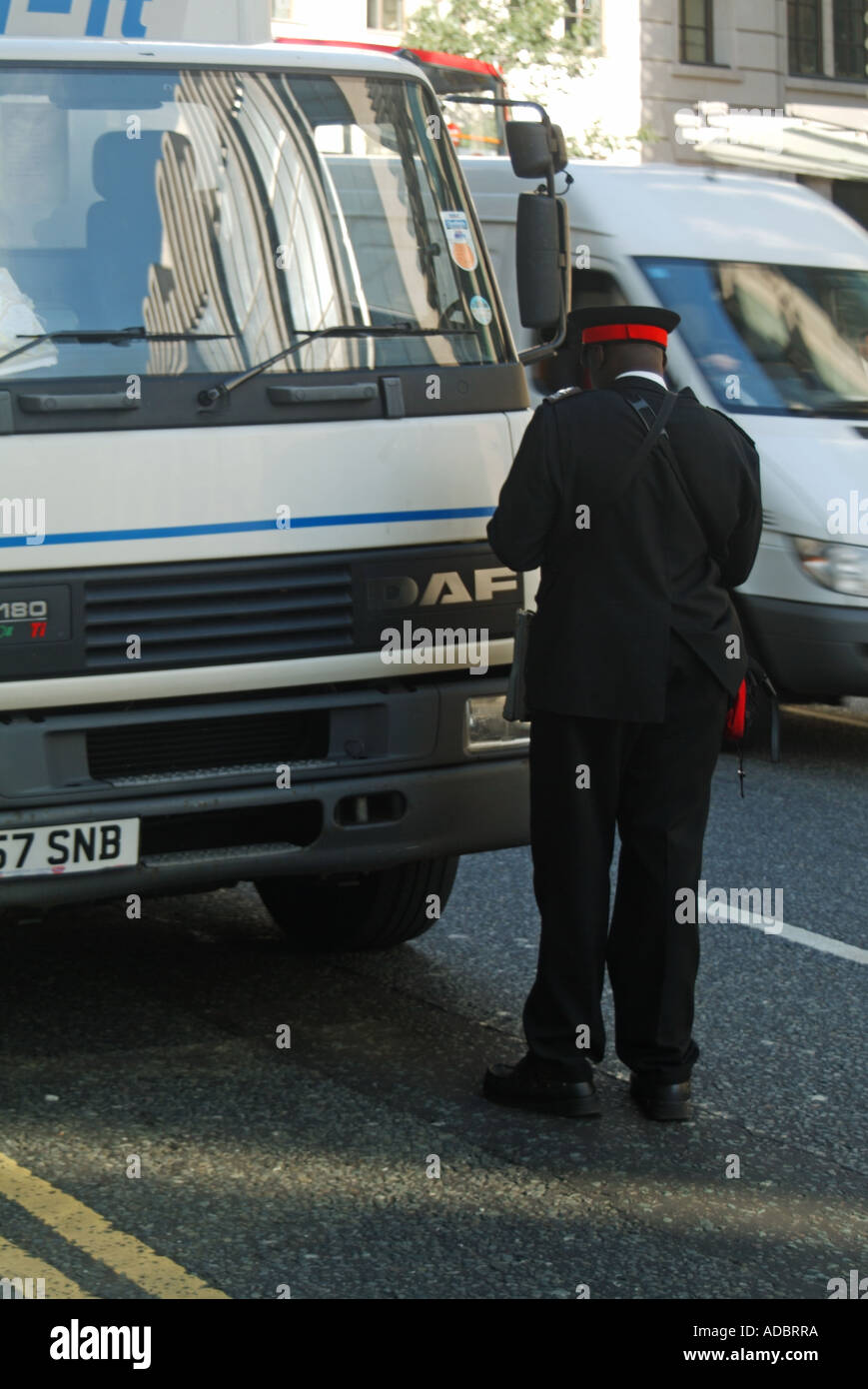 Scène de rue vue arrière garde-trafic en uniforme sur le point d'émettre un billet de stationnement pour camion stationné sur des lignes jaunes doubles City of London England UK Banque D'Images