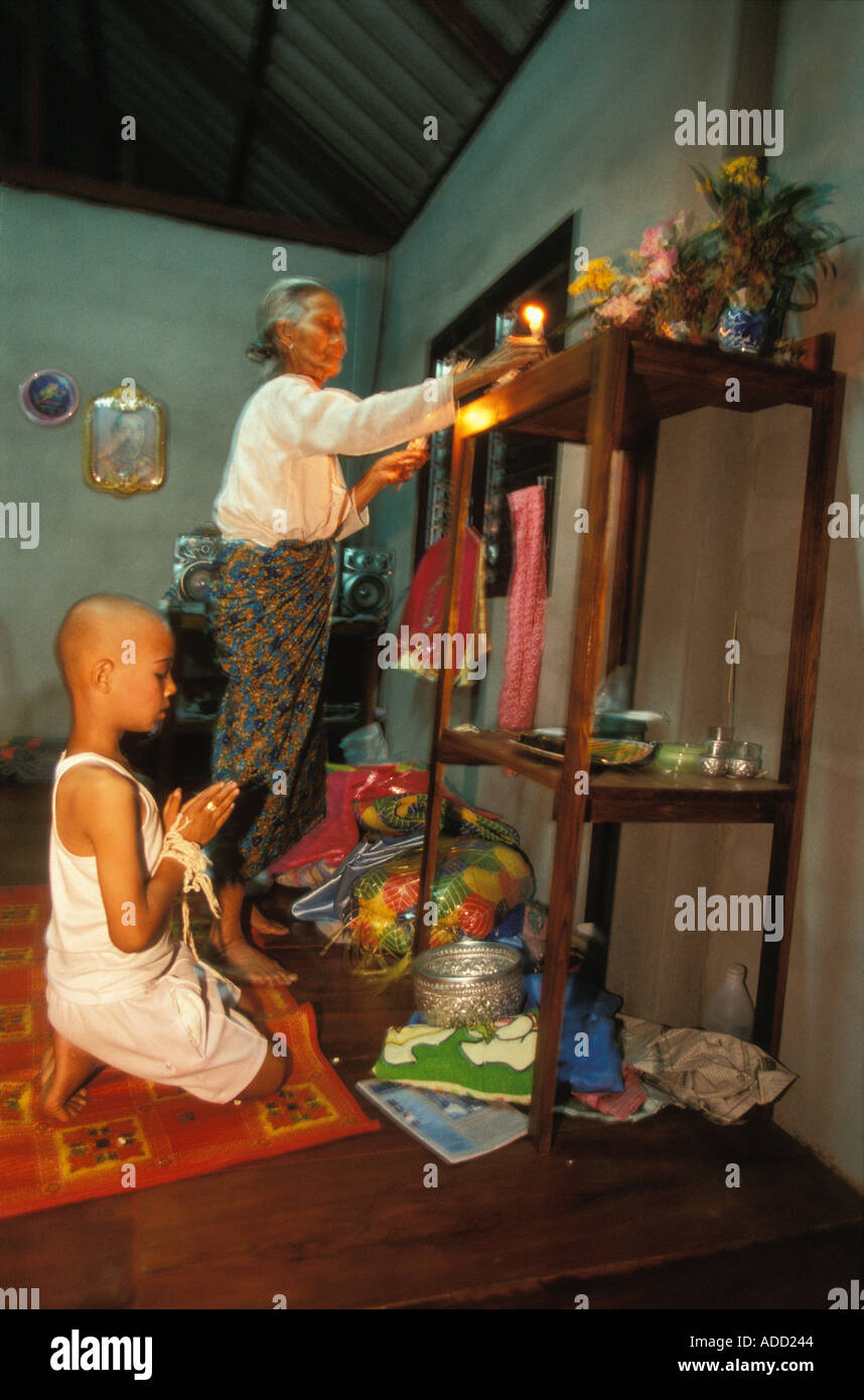 Garçon priant devant temple familial et grand-mère allumant des bougies le Poy a chanté longtemps Mae Hong Son, Thaïlande Banque D'Images