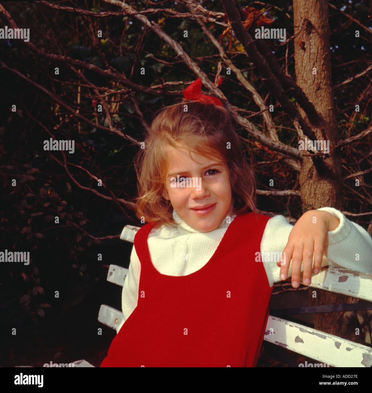 Jeune fille en rouge pinafore dress sur siège smiling at camera Banque D'Images