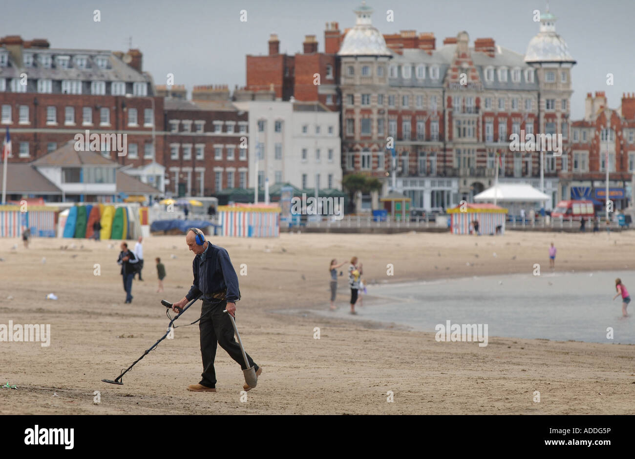 Un homme avec un détecteur de métal à monter et descendre la plage de Weymouth, Dorset, UK, à la fin de la journée. Banque D'Images