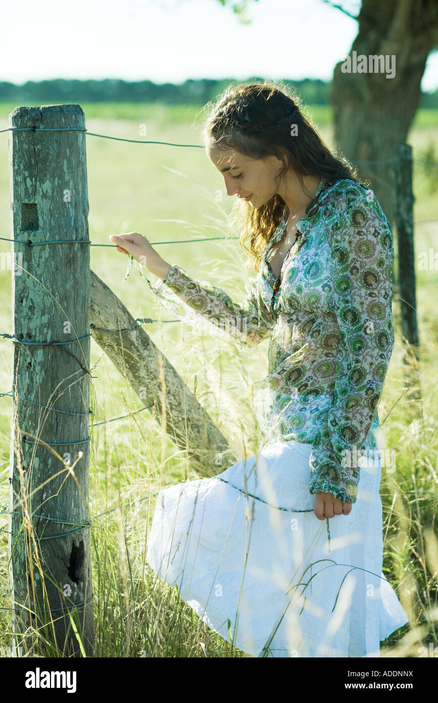Jeune femme debout à côté d'une clôture rurale, regardant vers le bas Banque D'Images