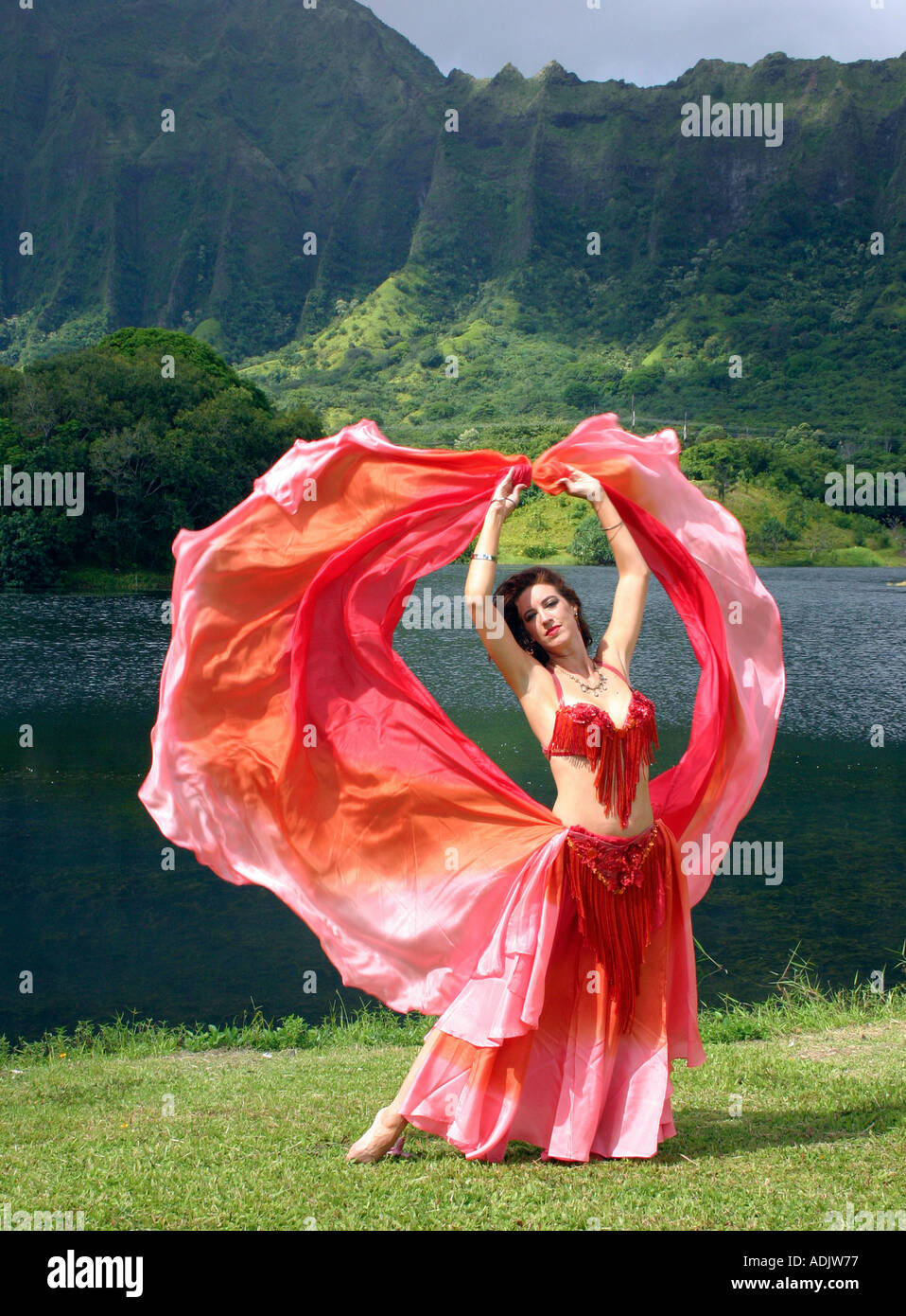 Danseuse du Ventre avec voile rouge, bras tendus au décor tropical Banque D'Images