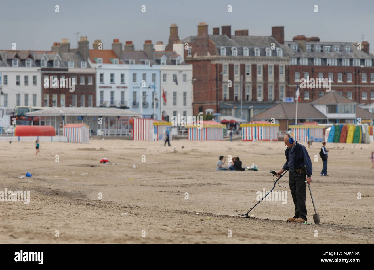 Un homme avec un détecteur de métal à monter et descendre la plage de Weymouth, Dorset, UK, à la fin de la journée. Banque D'Images