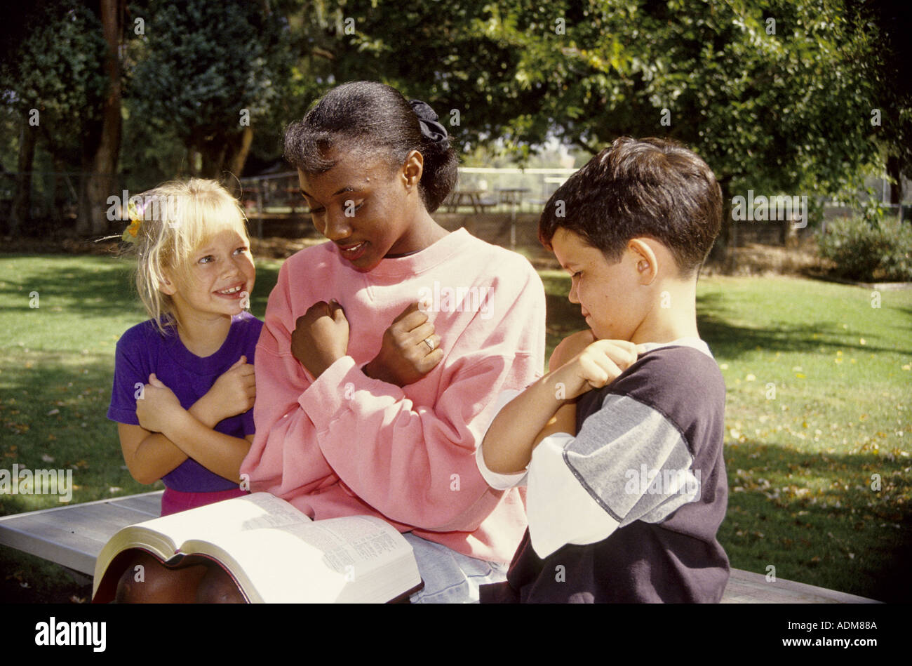 Deux jeunes enfants multiculturelle 'Amour' d'apprentissage pour l'apprentissage de la langue des signes américaine africaine adolescente comme elle lit la lecture de Bible United States Banque D'Images