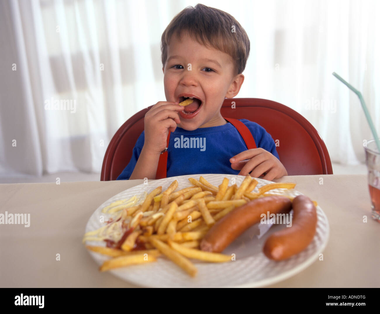 Petit garçon est en train de manger des frites et des saucisses avec de la mayonnaise Banque D'Images