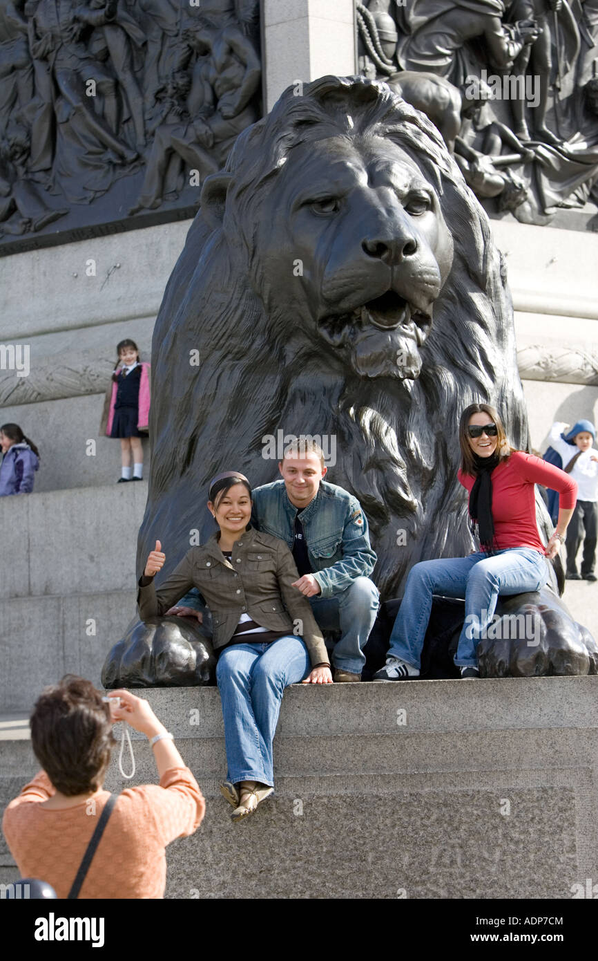 Des touristes posent pour des photos sur lion statue à la base de la Colonne Nelson de Trafalgar Square London UK Banque D'Images