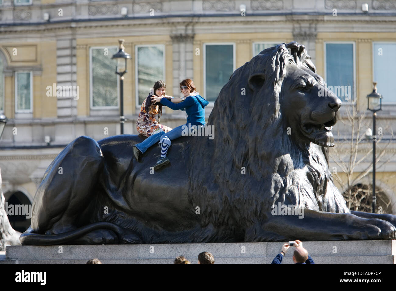 Des touristes posent pour des photos sur des statues de lion à Trafalgar Square London UK Banque D'Images