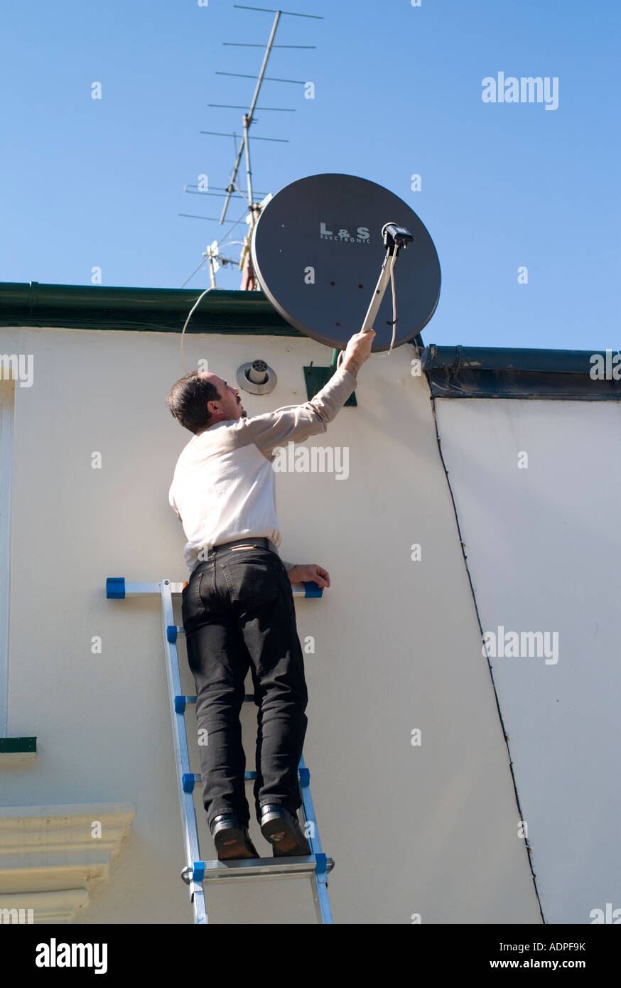 Homme debout sur une échelle, réglage de l'antenne récepteur TV par  satellite sur le mur d'une maison mitoyenne Photo Stock - Alamy
