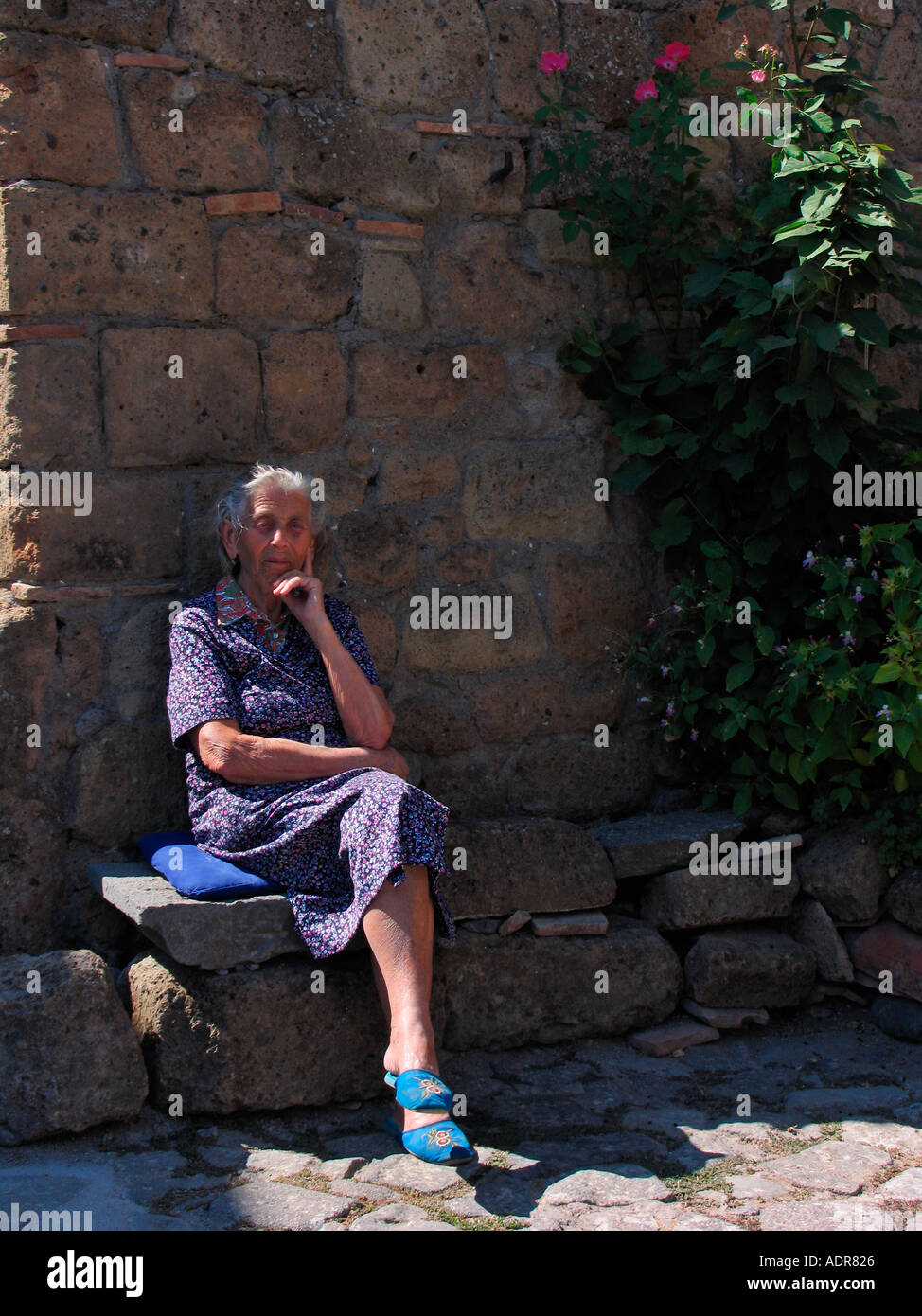 Femme assise sur le banc de pierre près de l'entrée de la Vittoria Antico Mulino moulin restaurant à Civita di Bagnoregio Italie Banque D'Images