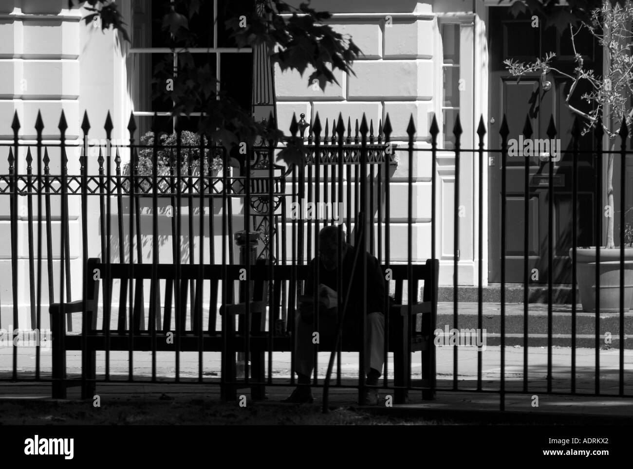 L'homme sur le banc vu derrière park garde-corps. Fitzroy Square, Fitzrovia, Londres, Angleterre Banque D'Images