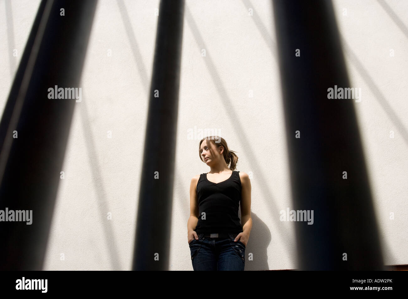 Jeune femme à l'intérieur avec les ombres de formes graphiques casting windows sur mur derrière elle à la cage ou comme une prison Banque D'Images