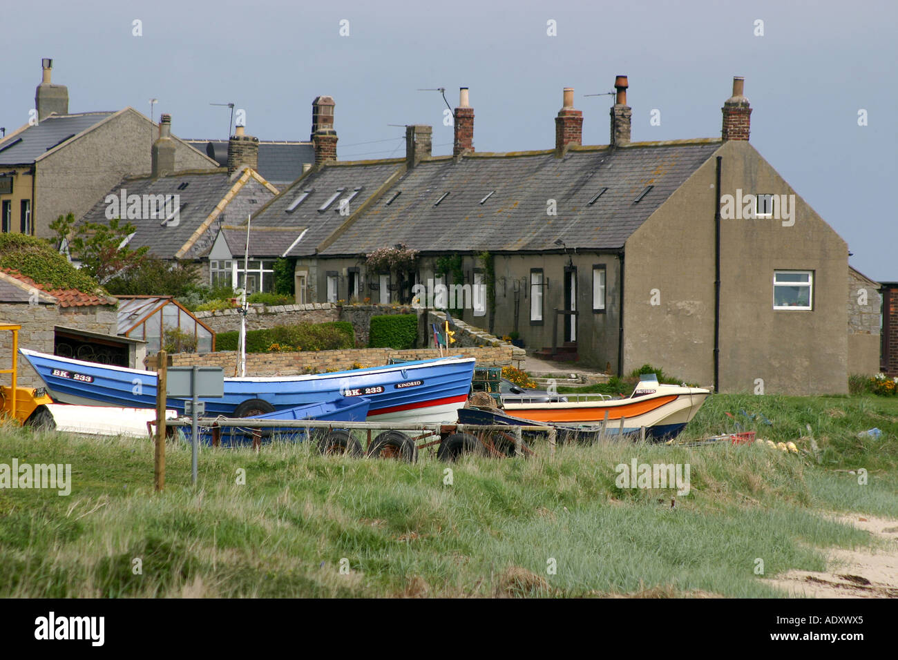 Groupe de chalets sur la côte de Northumberland avec bateaux de pêche sur la terre près d'eux. Banque D'Images